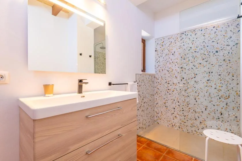 A bright bathroom with a vanity, mirror, and tiled shower area.