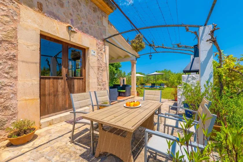 An outdoor dining area with a long table and chairs beneath a blue shade canopy.