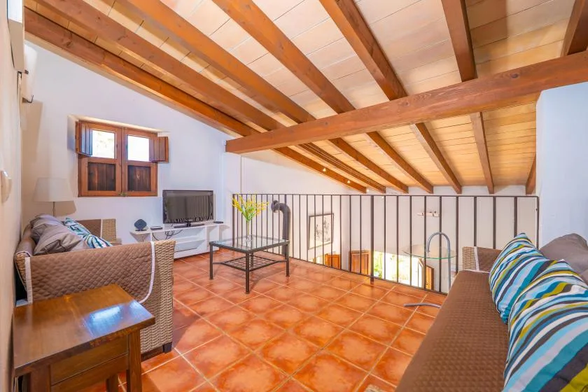 A loft-style living area has exposed wooden beams, seating, and a television.