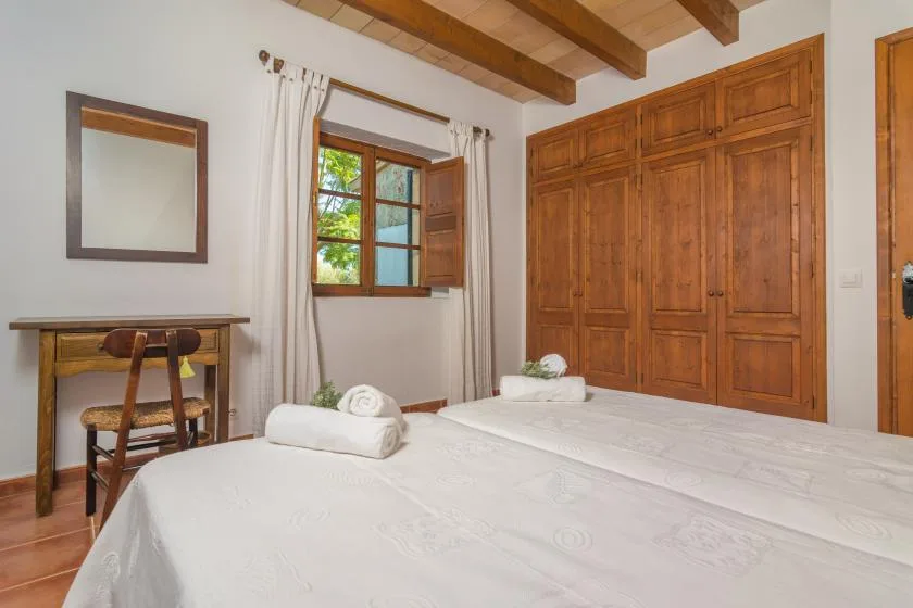 A bedroom with white bedding, a wooden wardrobe, and a window with curtains.