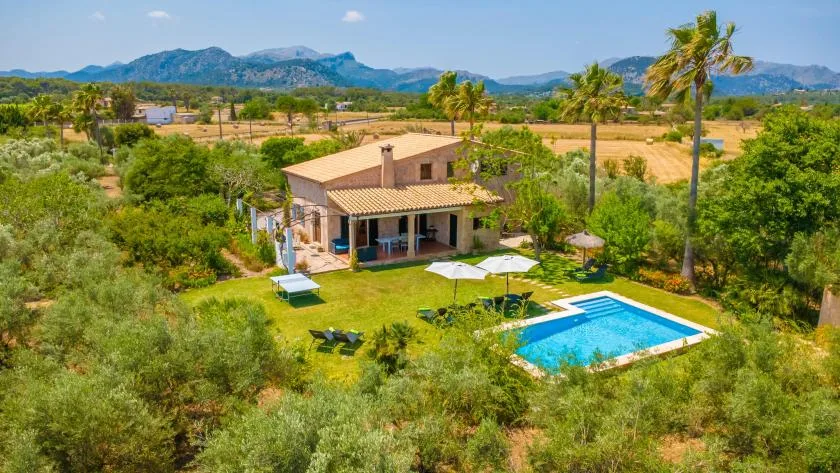 A countryside house stands beside a swimming pool amid green gardens.