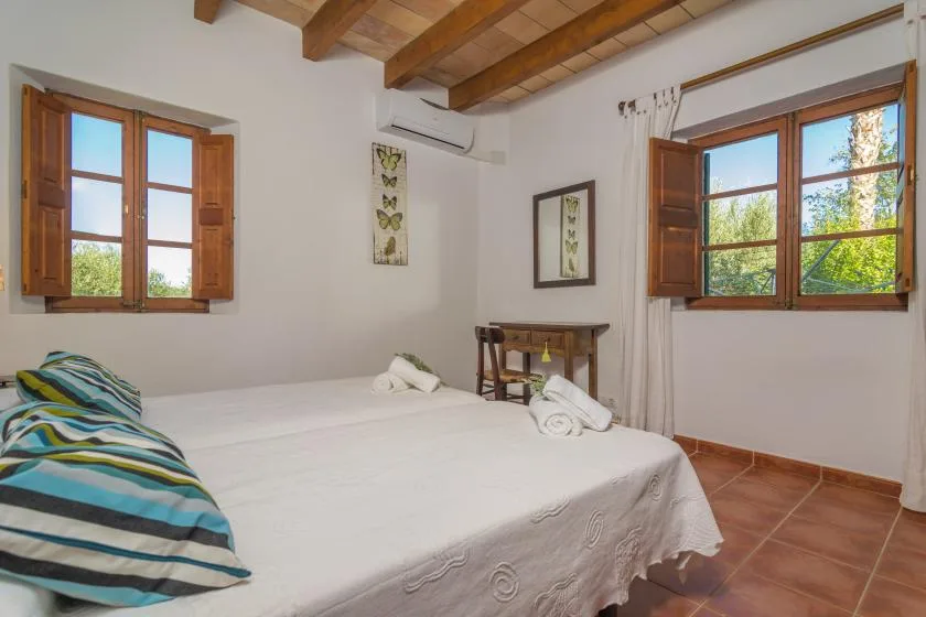A bedroom with a bed, wooden ceiling beams, and windows overlooking greenery.