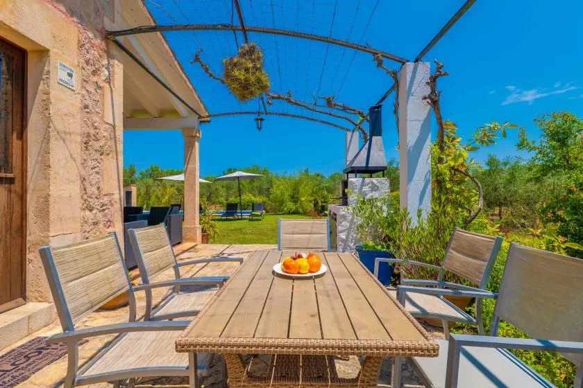 An outdoor dining area with a long table and chairs beneath a pergola.