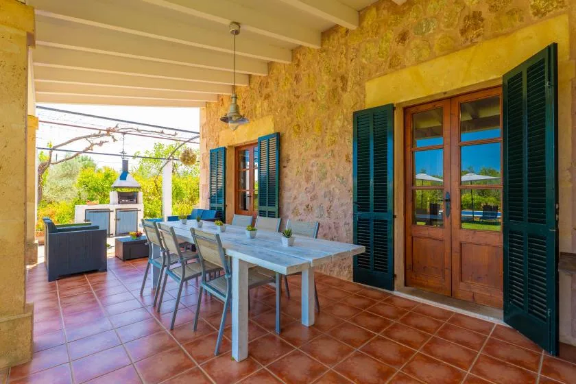 A covered outdoor dining area with a long table and blue shutters.