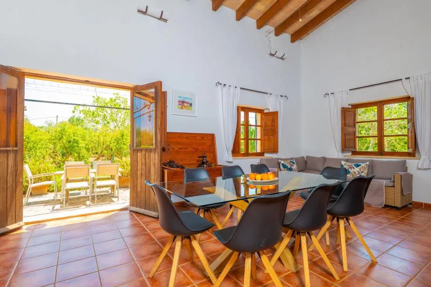 A bright dining and living area with a long table and open doors to a patio.