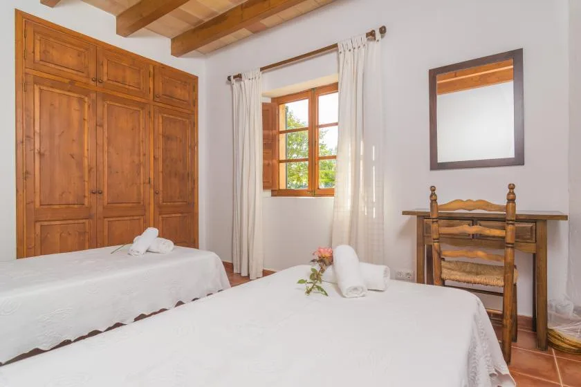 A bedroom with two beds, a wooden wardrobe, and a window with light curtains.