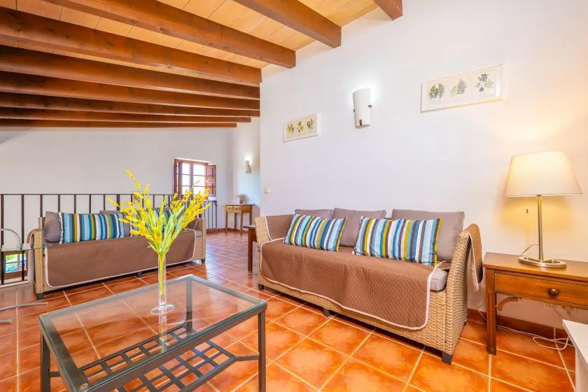 A living room with two seating areas, a glass coffee table, and exposed wooden ceiling beams.