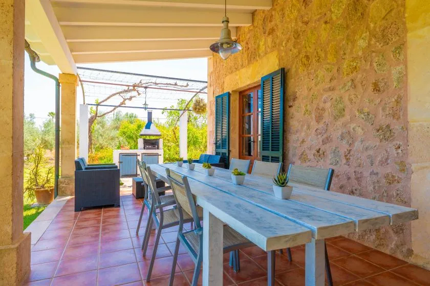 A covered patio with a long outdoor dining table beside a stone wall.