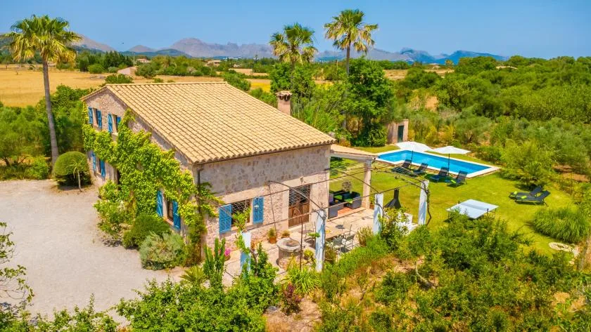 A stone house and swimming pool sit among gardens with hills in the distance.