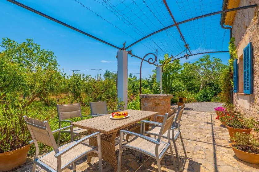 An outdoor patio dining area sits beneath a blue canopy, surrounded by garden greenery.
