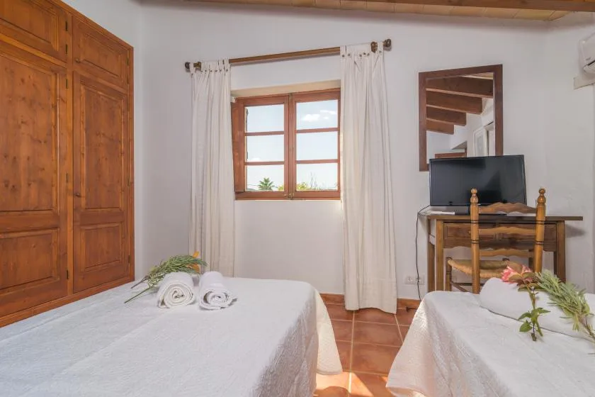 A bedroom with two beds, a window, and a wooden wardrobe.