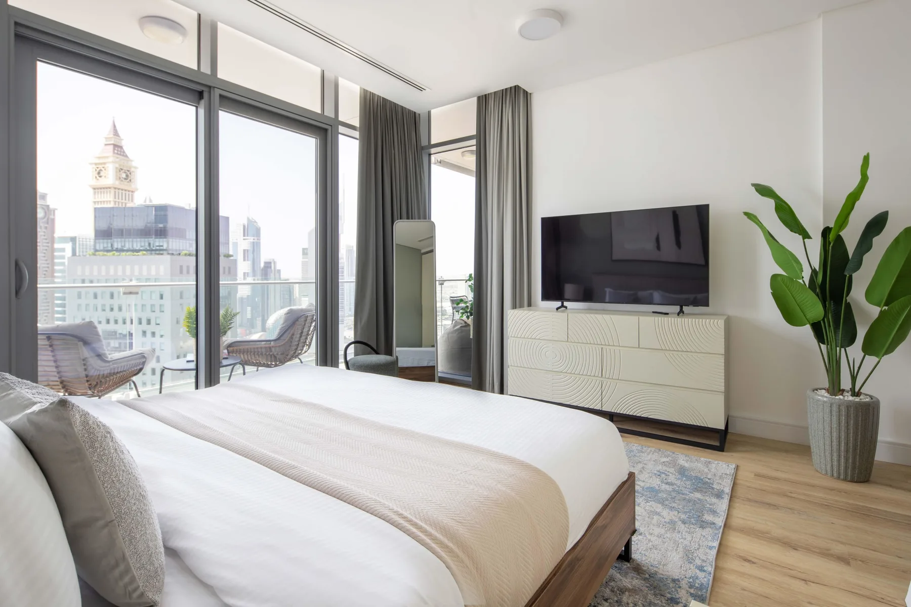 A bright bedroom with floor-to-ceiling windows, a bed, and a television.