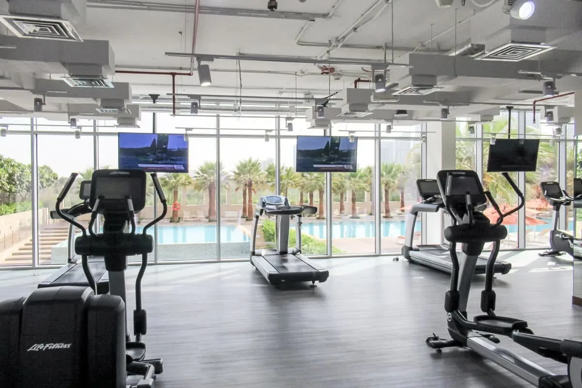 A fitness room with exercise machines and large windows overlooking a pool.