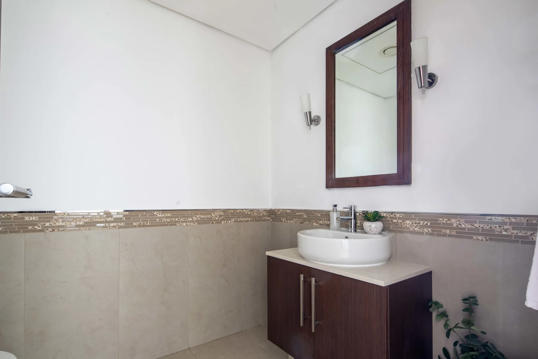 A bathroom with a sink vanity, wall mirror, and tiled walls.