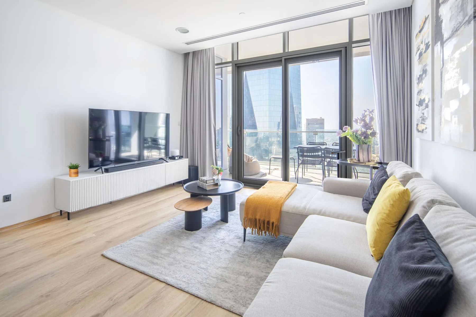 A bright living room with seating, a television, and glass doors opening onto a balcony.
