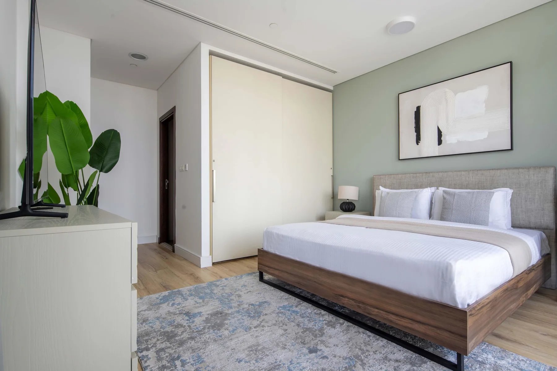 A bedroom with a large bed, a pale green wall, and a framed artwork.