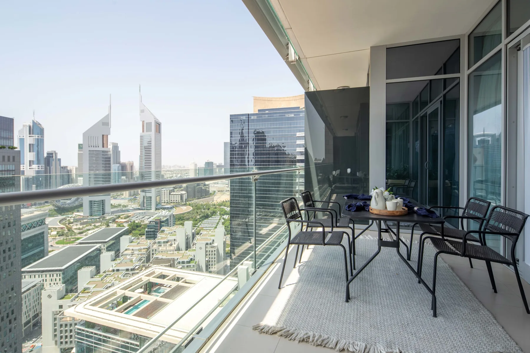 A balcony seating area overlooks a city skyline, with a table beside the glass railing.