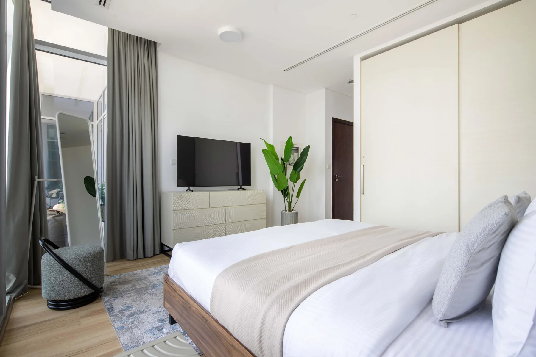 A bright bedroom with a bed, television, and potted plant.