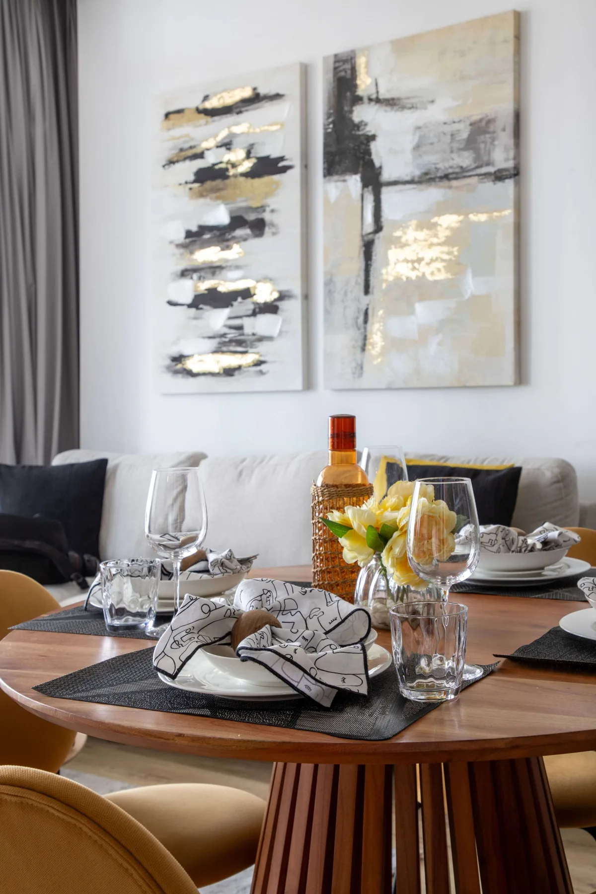 A dining table set with glassware and dishes sits beneath abstract wall art.