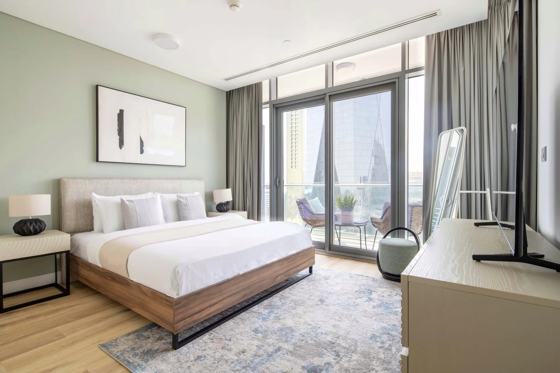 A bright bedroom with a large bed beside floor-to-ceiling windows.