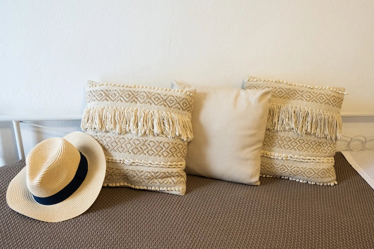 A bed with patterned cushions and a straw hat resting on it.