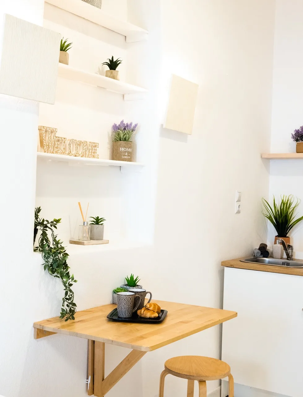 A bright dining nook features a wooden table and wall shelves with plants.