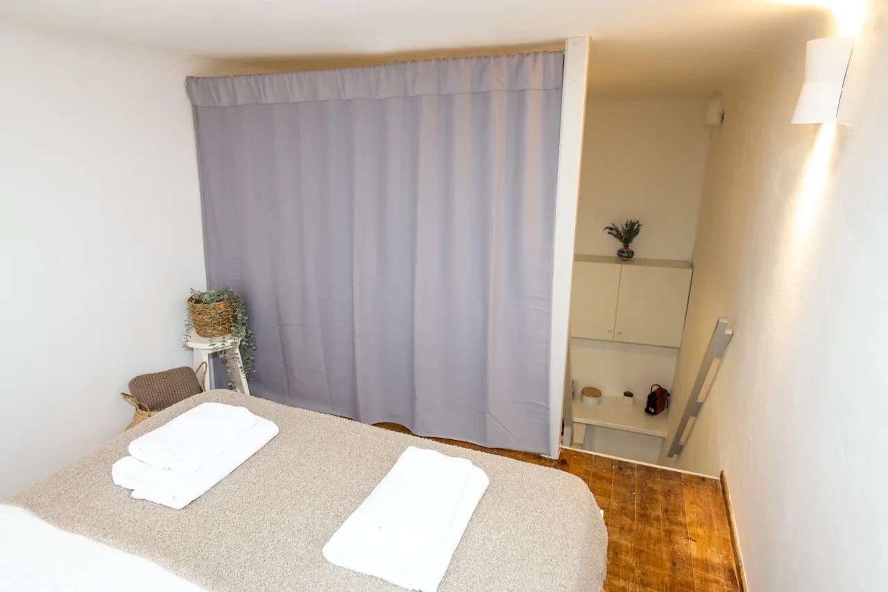 A bedroom with a bed, folded towels, and a curtain screening a small alcove.