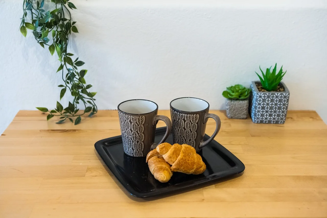 A wooden countertop displays a tray with two mugs and pastries.