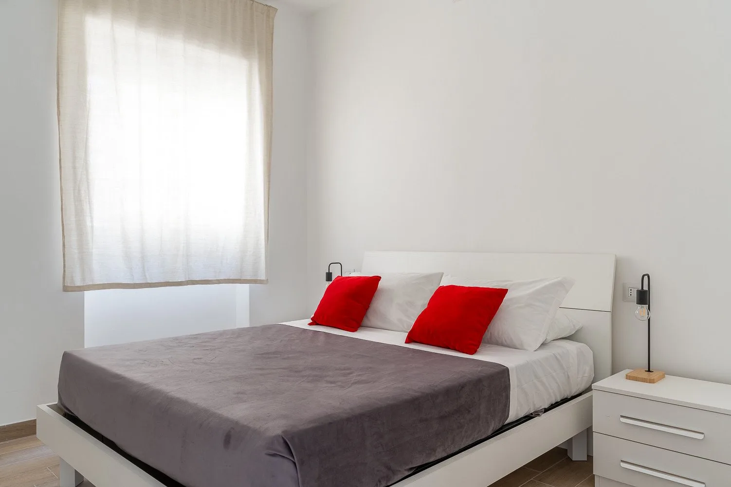 Un dormitorio con una cama vestida con ropa de cama gris y una ventana luminosa.