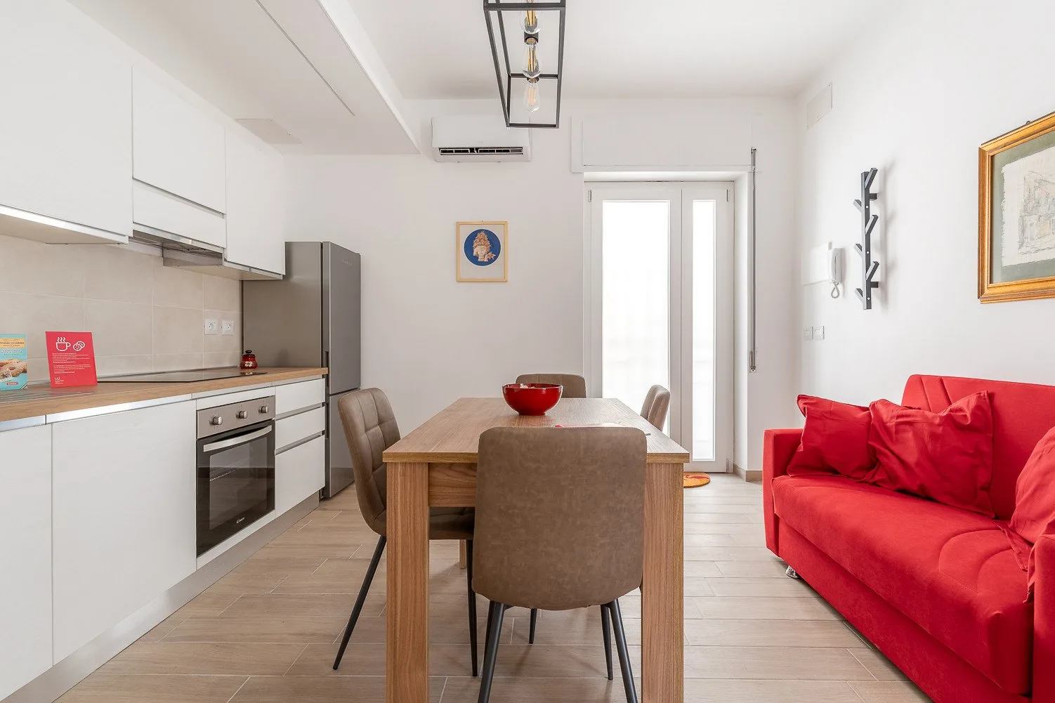 Una luminosa zona de comedor y estar con una mesa de madera y asientos rojos.