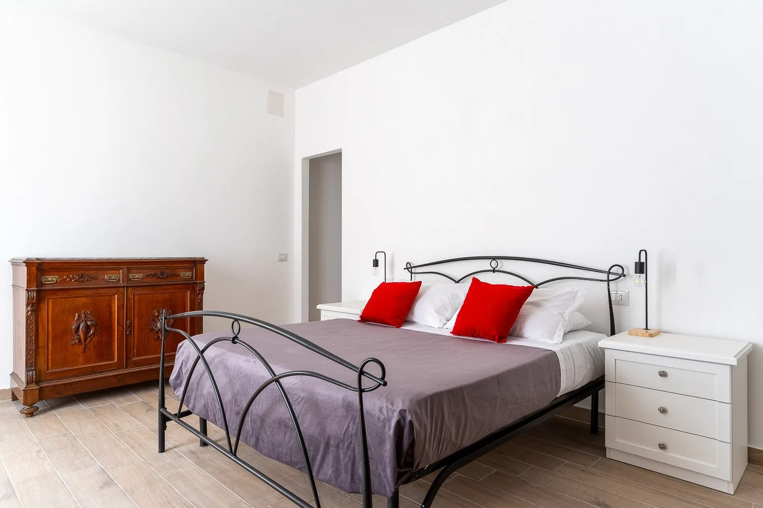 Un dormitorio luminoso con una cama de metal, cojines rojos y mesitas de noche.