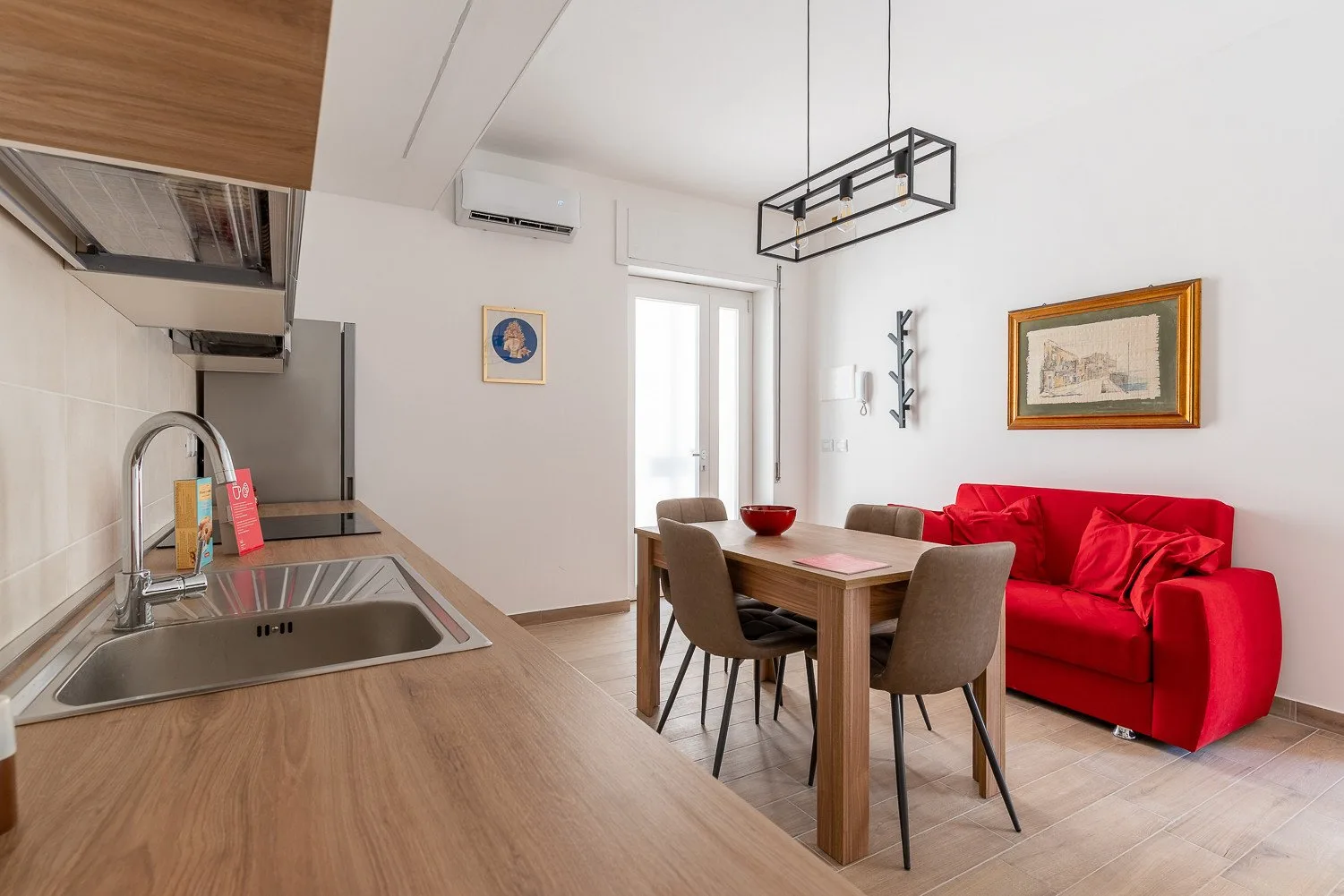 Una cocina y zona de comedor luminosa, con una mesa junto a un sofá rojo.