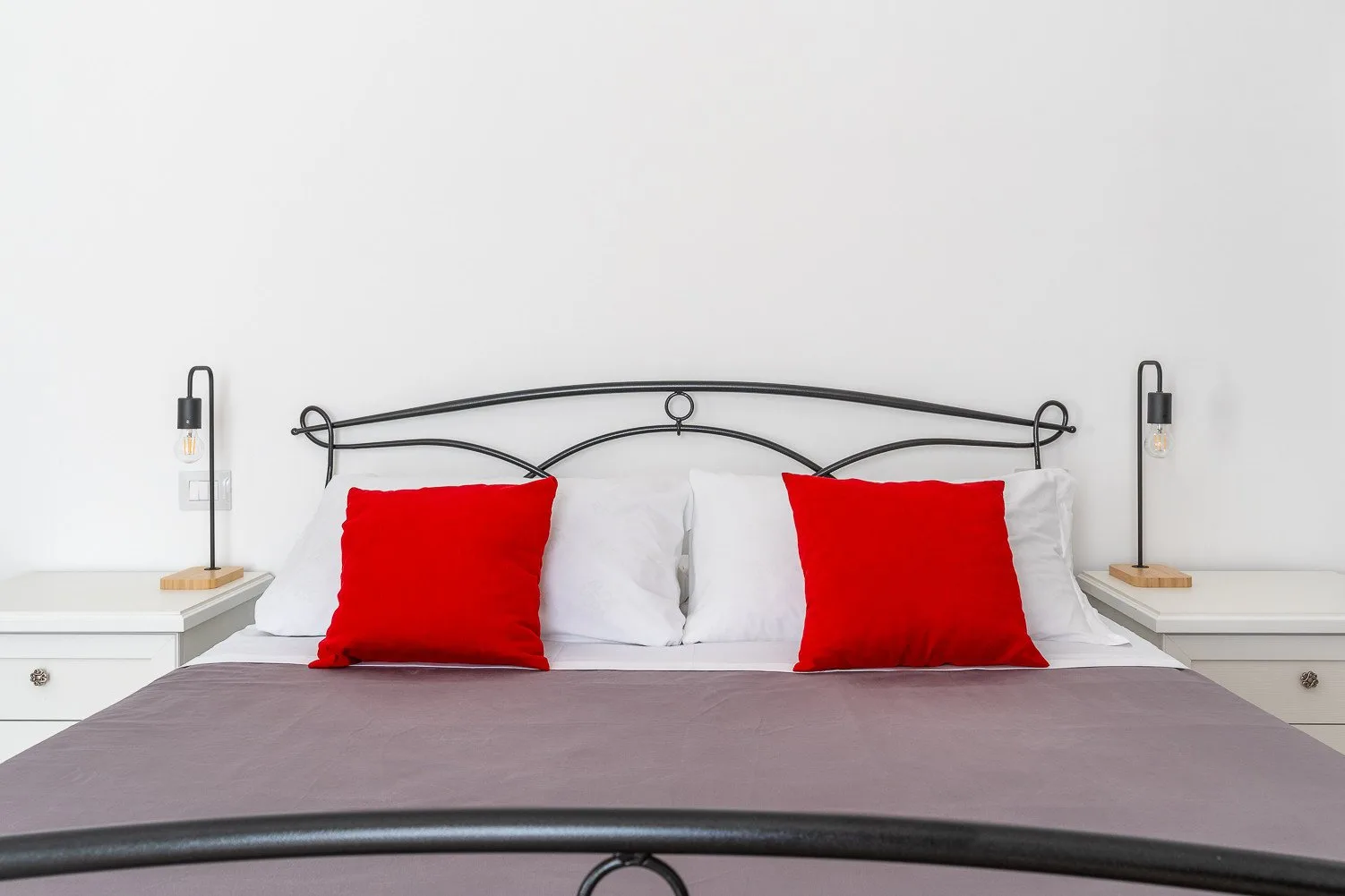 Un dormitorio con una cama ordenada, almohadas blancas y cojines decorativos rojos.