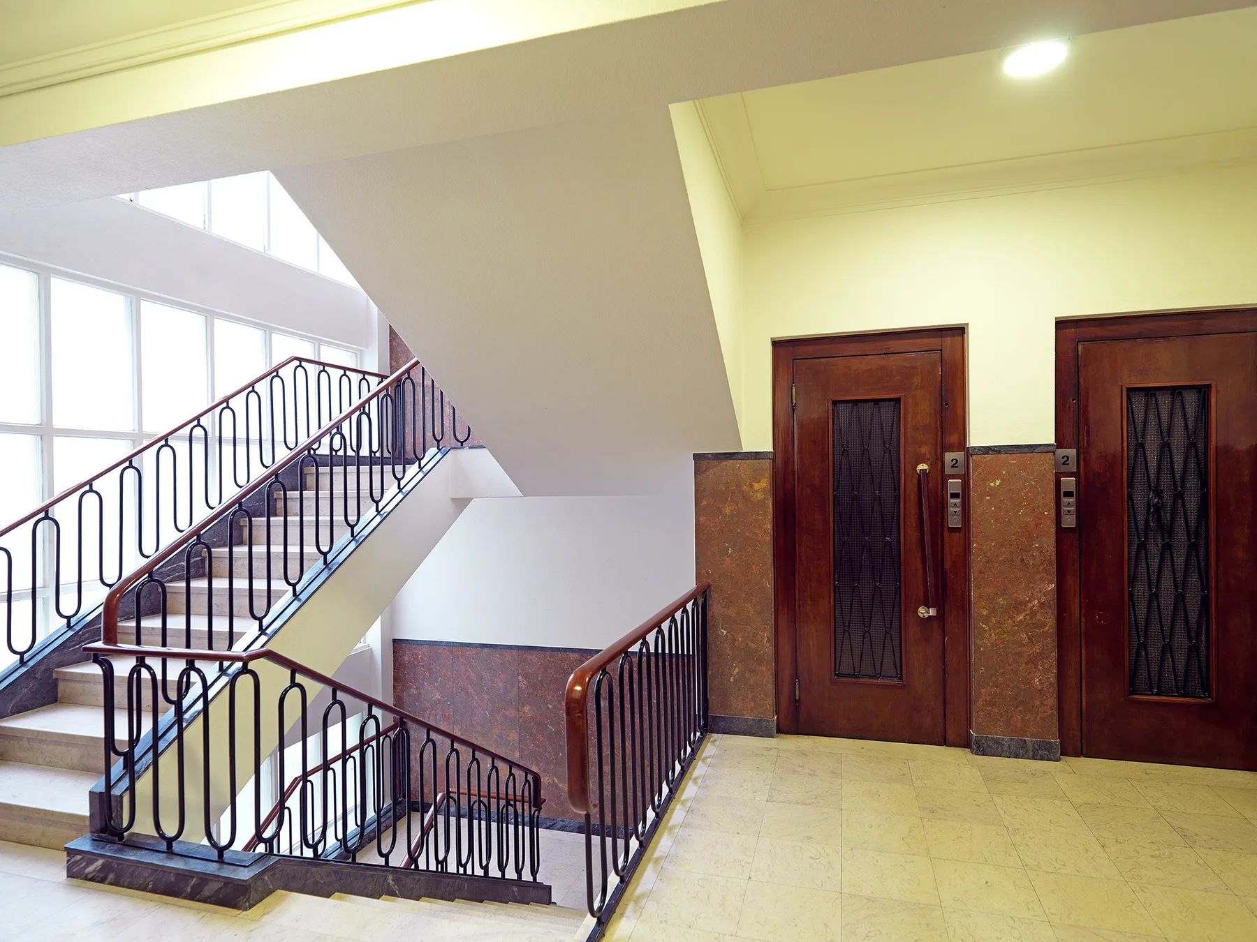 Una escalera interior con barandillas metálicas y dos puertas de ascensor de madera.