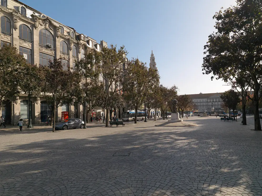 Una amplia plaza pavimentada está bordeada de árboles y edificios de varias plantas.