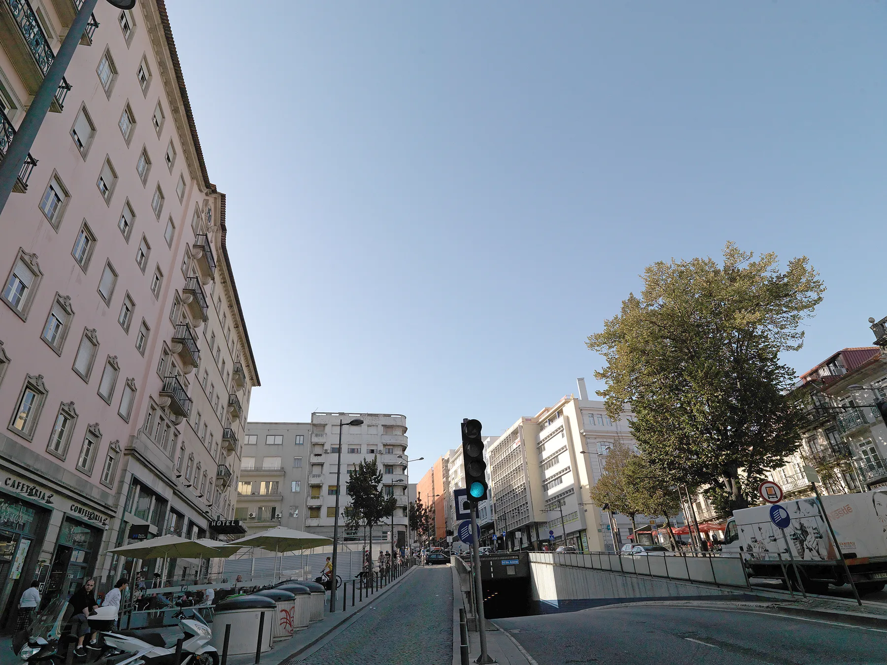 Una escena urbana con edificios de varios pisos, un semáforo y un árbol grande.