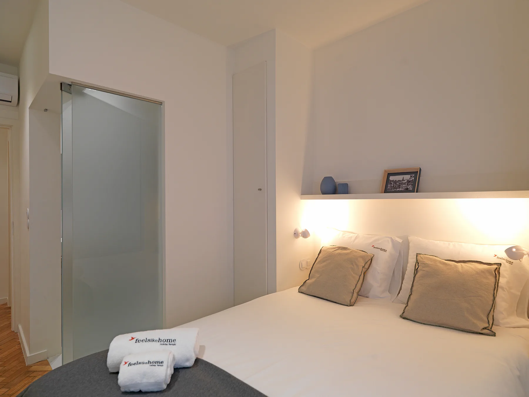 Un dormitorio con una cama, almohadas y una repisa iluminada.