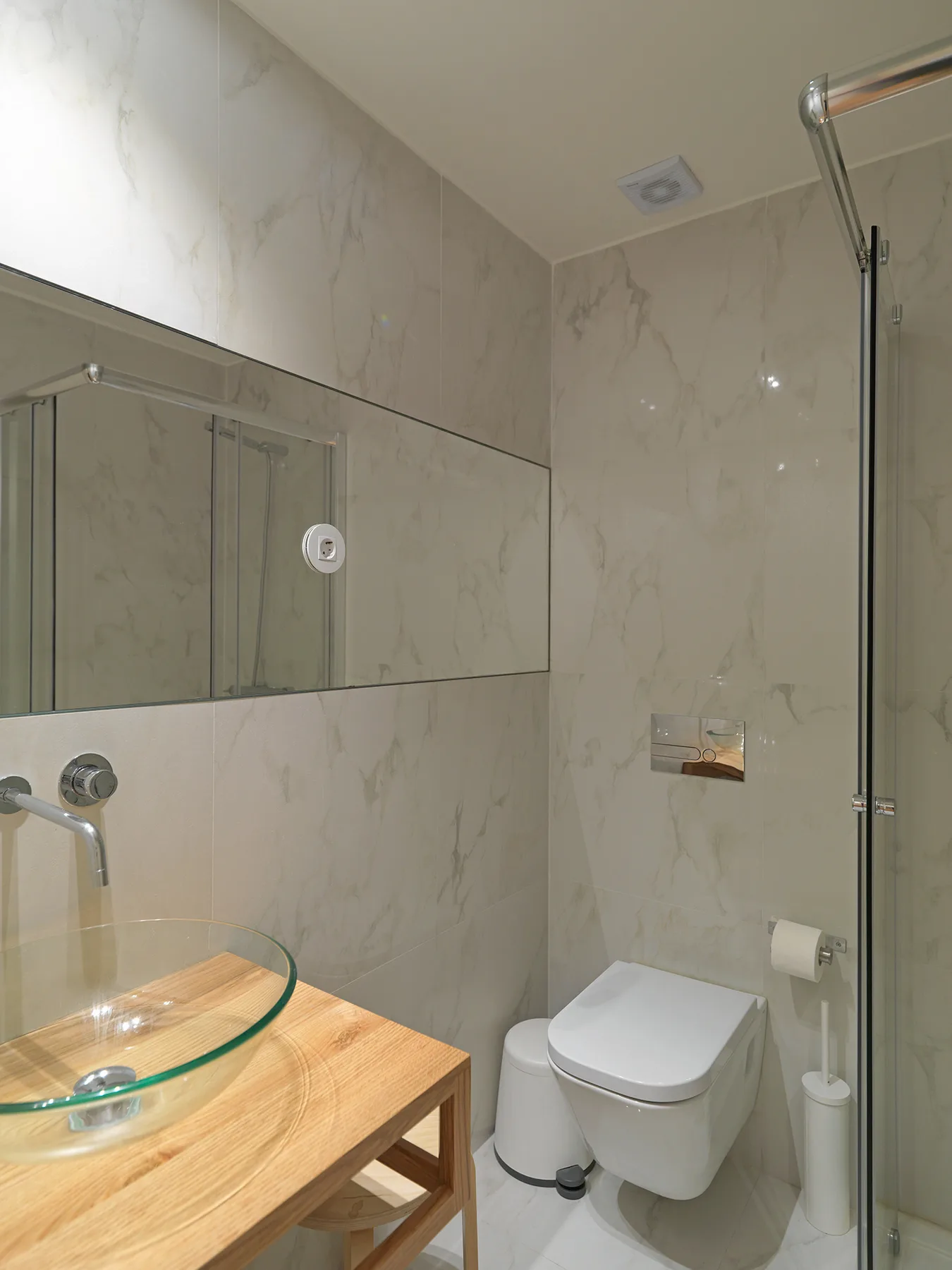 Un baño con lavabo de vidrio, inodoro y mampara de ducha de vidrio.