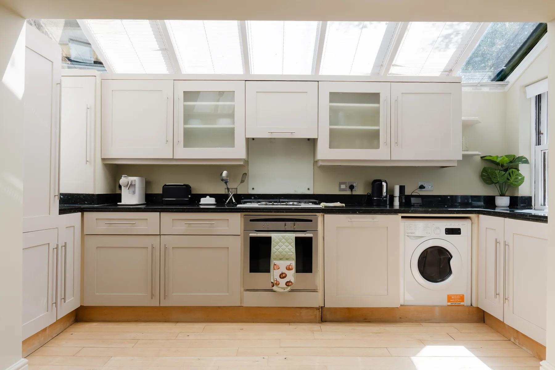 A bright kitchen with pale cabinets beneath a glass roof.