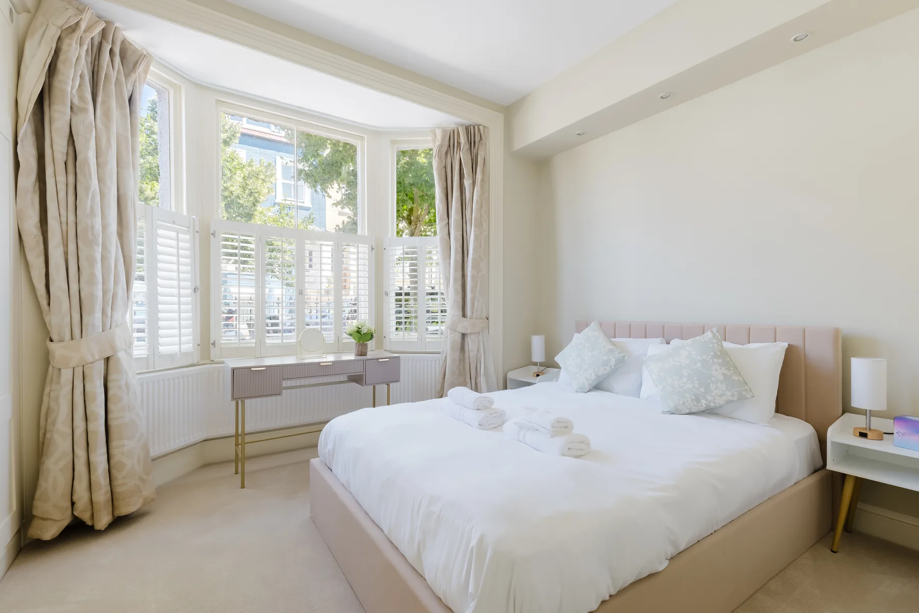 A bright bedroom with a white bed beside large windows.