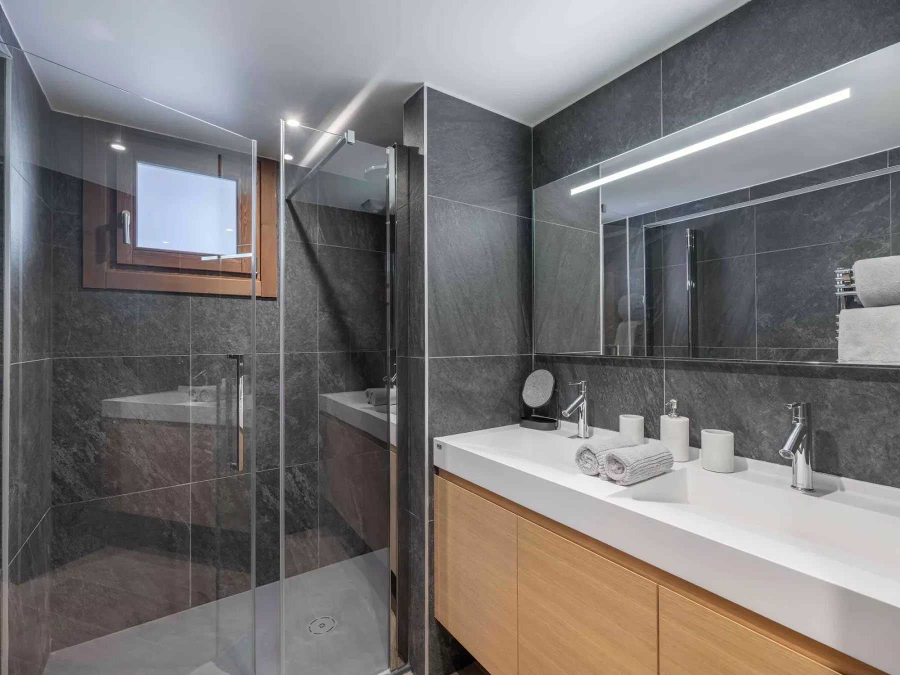 Un baño moderno con ducha de vidrio y un largo lavabo bajo un espejo.
