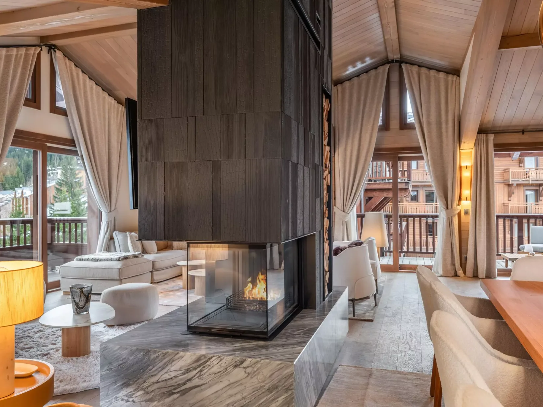 Una sala de estar con asientos alrededor de una chimenea central y grandes ventanales.