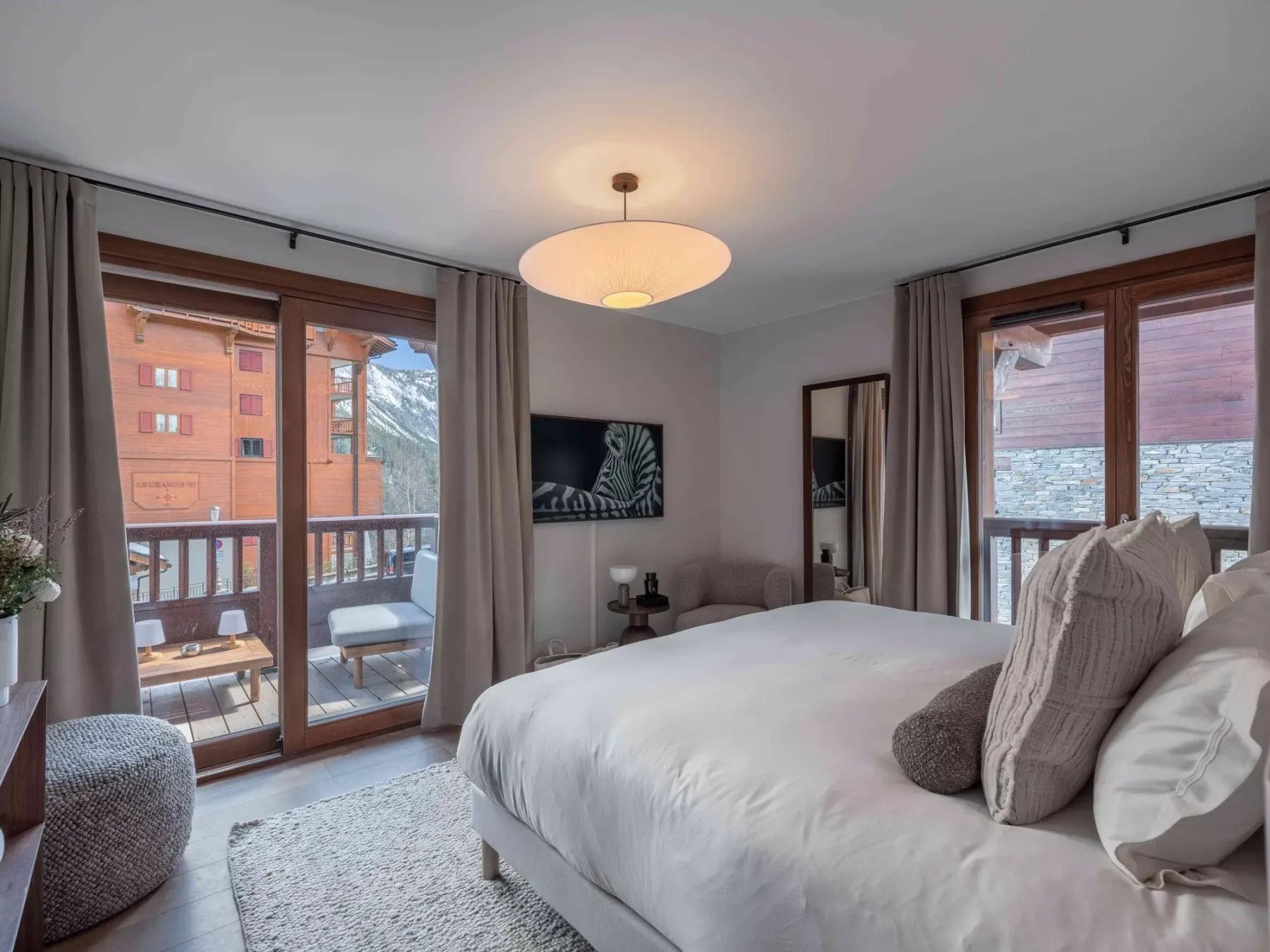 Un dormitorio con la cama tendida y grandes ventanas con vistas a un balcón.