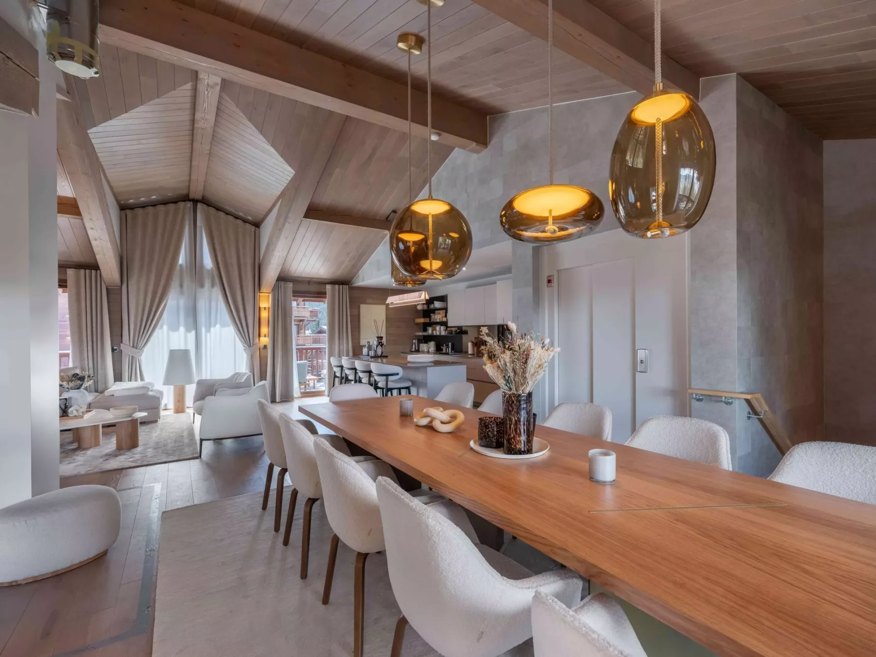 Un espacio abierto de comedor y cocina con una mesa larga de madera y lámparas colgantes.