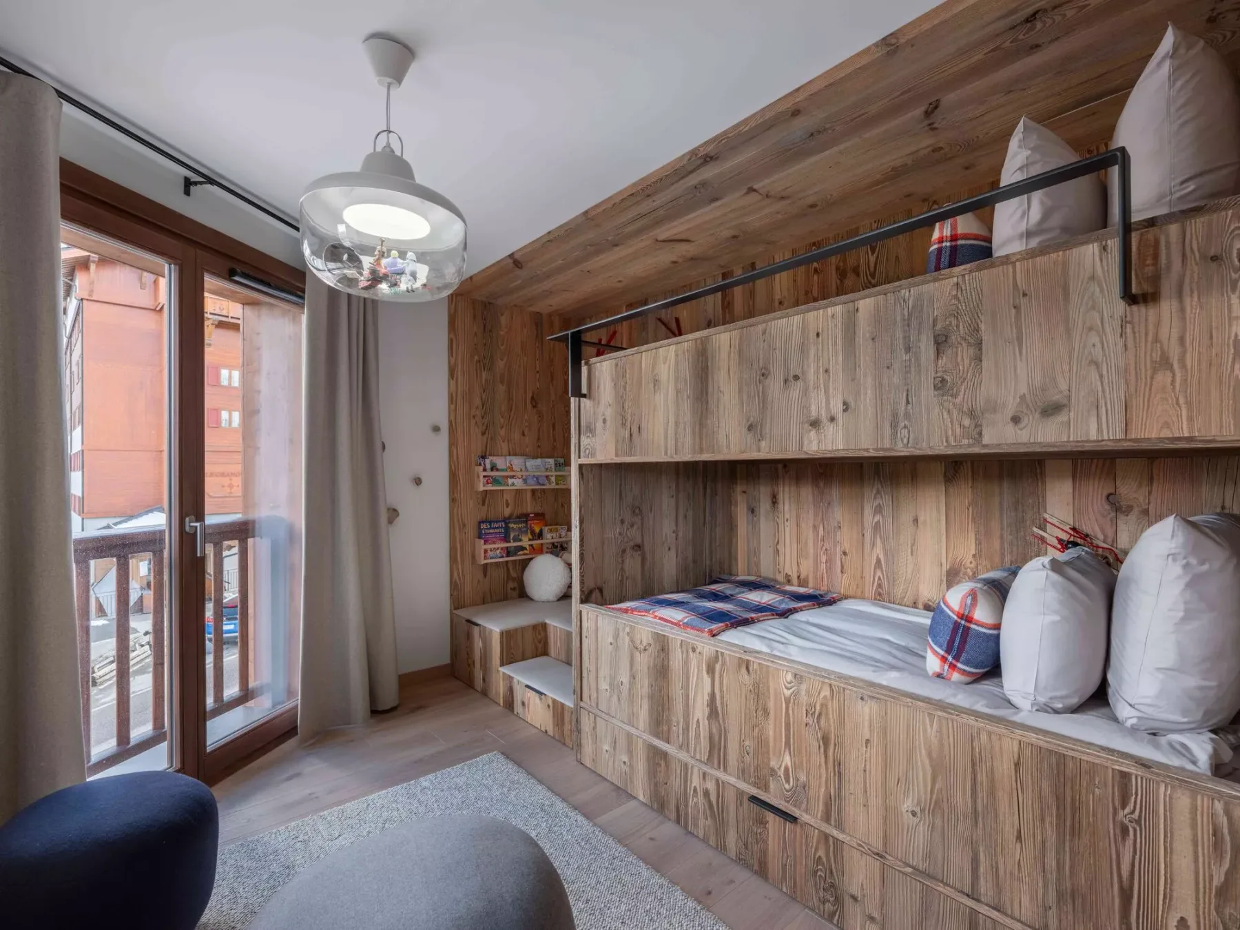Un dormitorio revestido de madera, con camas empotradas y una puerta acristalada que da a un balcón.