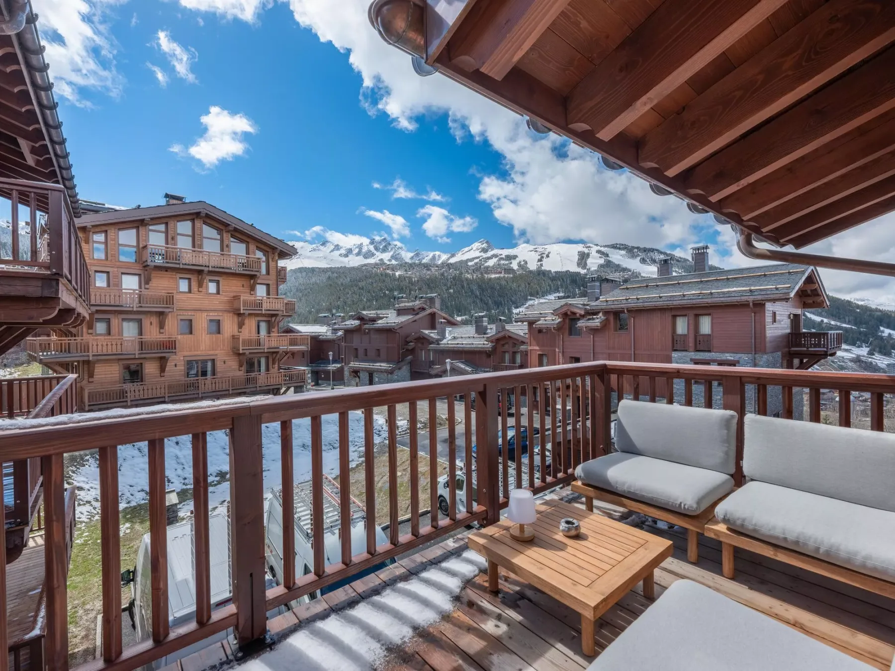 Un balcón amueblado da a edificios de madera y un paisaje montañoso con nieve.
