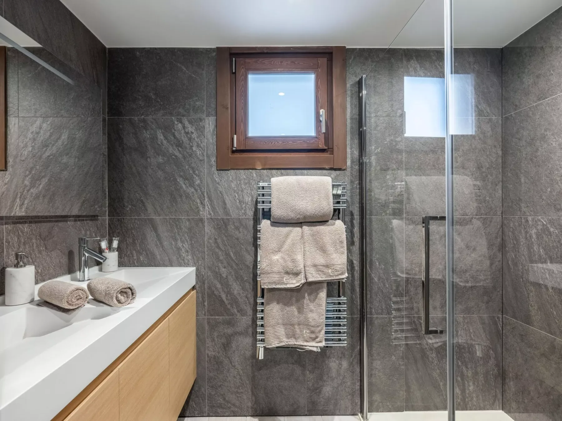 Un baño revestido de azulejos con lavabo, toallero y ducha de vidrio.
