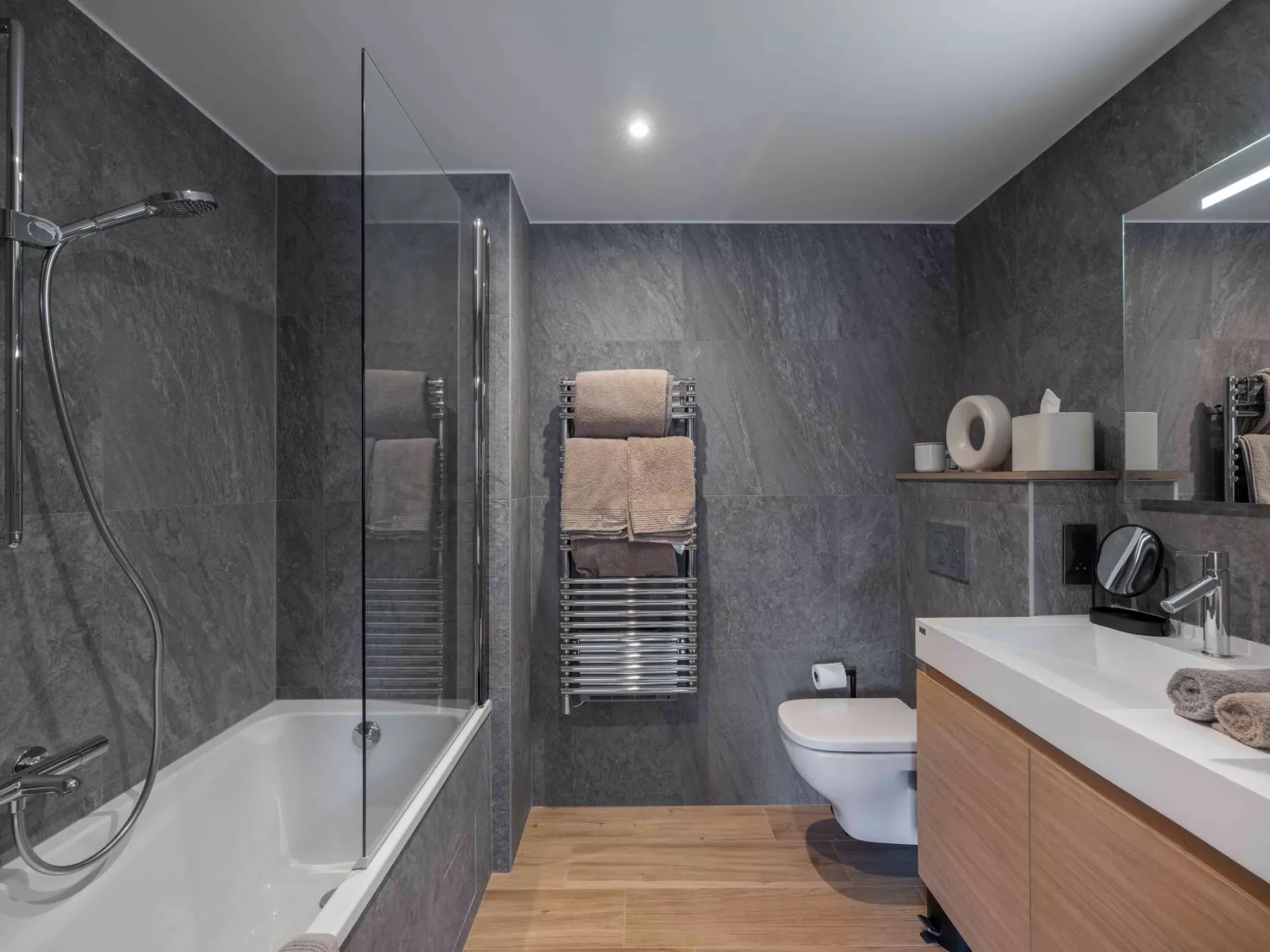 Un baño moderno con bañera, ducha, inodoro y mueble de acabado en madera.