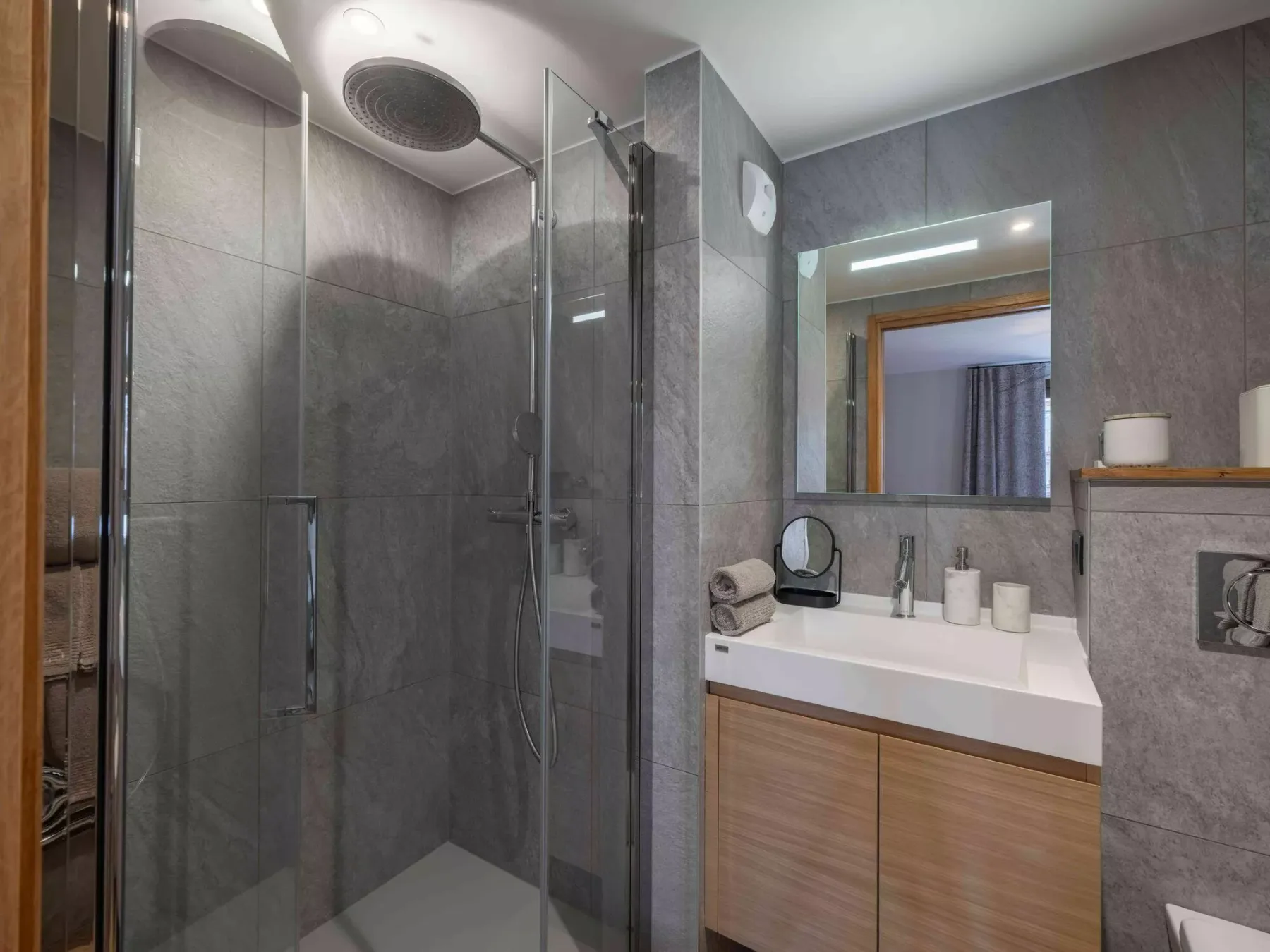 Un baño moderno con una ducha de vidrio y un lavabo bajo un espejo.