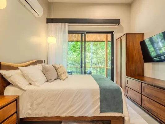A bedroom with a neatly made bed and a glass door opening onto greenery.